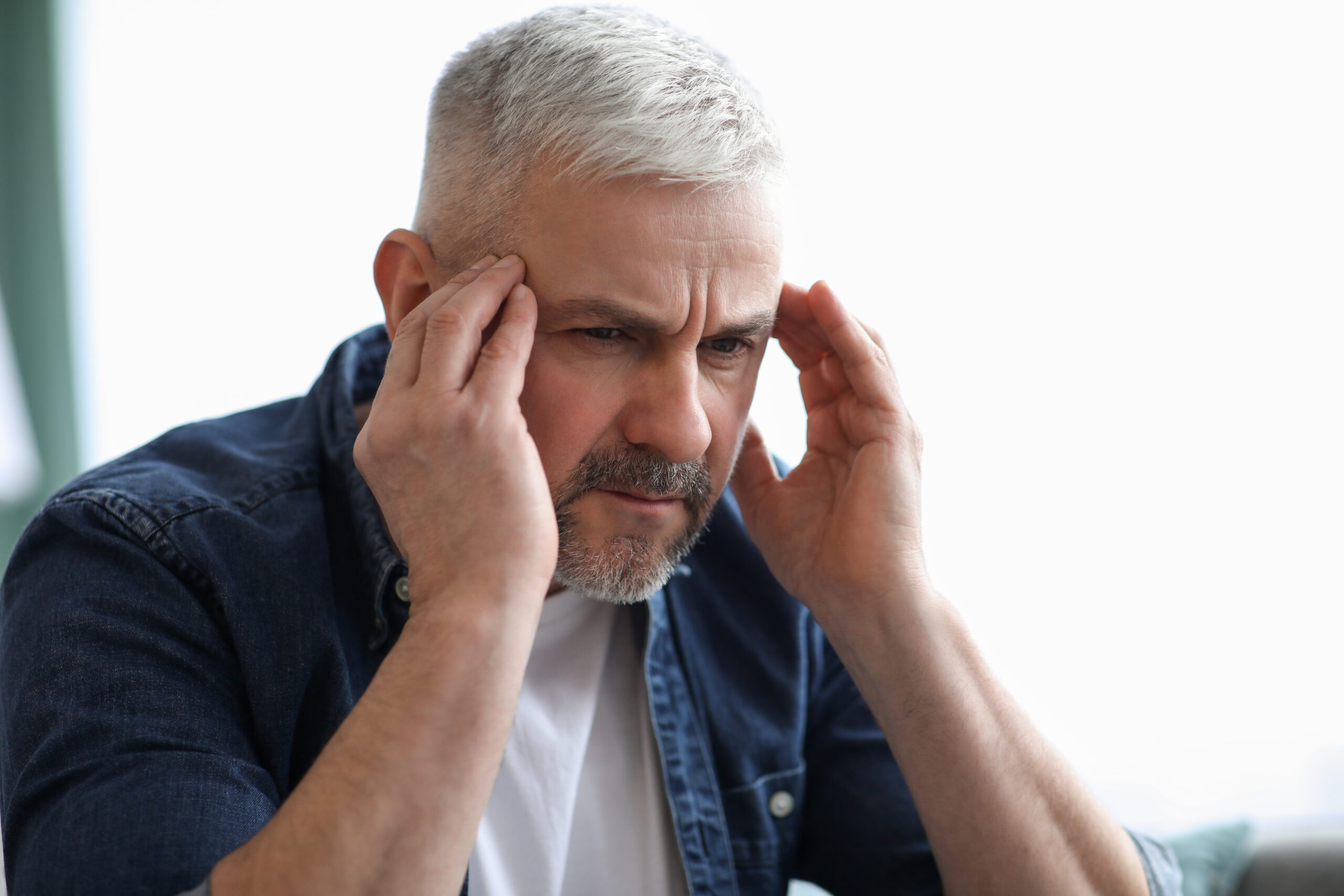 Closeup of mature grey-haired man suffering from migraine